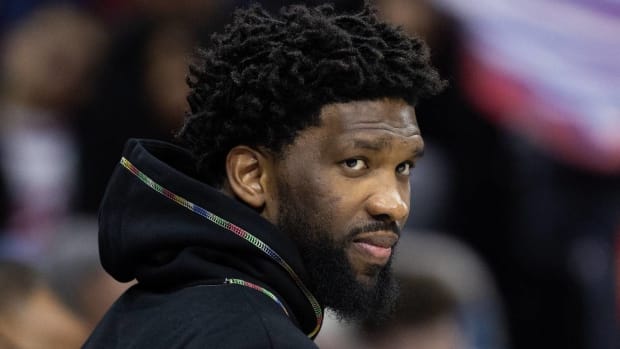 76ers center Joel Embiid looks on in street clothes during a game.